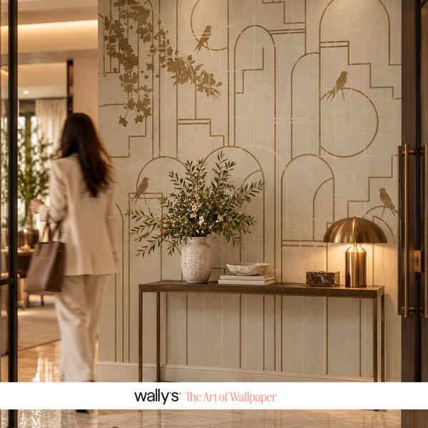 A woman in a light beige suit walks past a modern console table in a stylish interior. The wall behind her features elegant beige wallpaper with a gold geometric arch pattern and bird silhouettes.