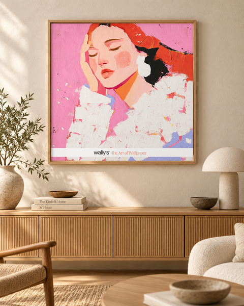 A framed art print featuring a stylized portrait of a woman with a red headscarf and white textured clothing on a pink background, displayed on a beige wall above a wooden console table in a modern living room setting.