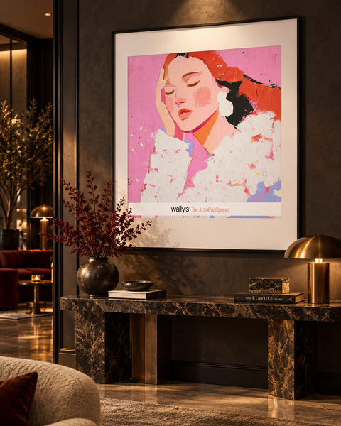 A framed art print featuring a stylized portrait of a woman in pink, red, and white tones, displayed on a dark wall above a marble console table in a modern, warmly lit interior setting.