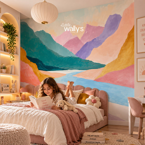 A child reads on a bed in a cozy bedroom featuring a large colorful mountain landscape wall mural. The room includes a pink bed, plush toys, a hanging paper lantern, built-in shelving with books and plants, and framed wall art.