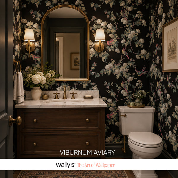 Bathroom with dark floral bird wallpaper, marble countertop and gold mirror.