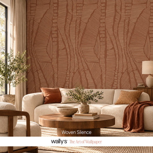 A styled living room featuring a large wall of wallpaper with a warm terracotta and brown abstract leaf-like line pattern. In front of the wall is a cream sofa with rust and beige pillows, a round wooden coffee table, and plants.