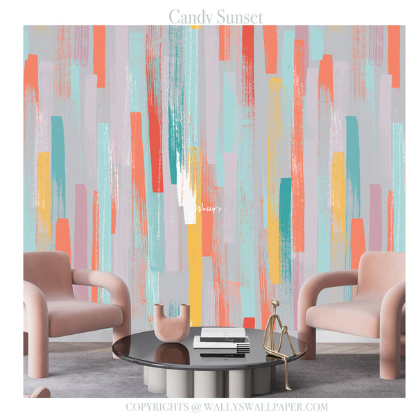 Abstract wall mural wallpaper with vertical brushstroke patterns in coral, teal, yellow, pink, and lavender on a light gray background, shown in a styled living room setting with two blush pink armchairs and a round black coffee table.