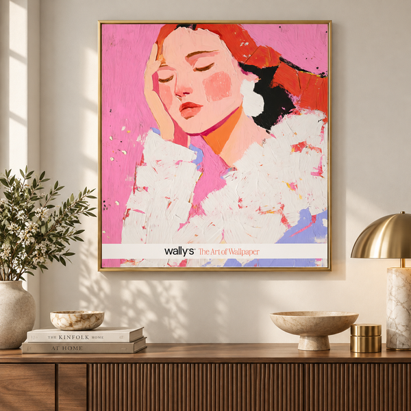 A framed wall art print featuring a stylized portrait of a woman in pink, red, white, and blue tones, displayed above a wooden console table in a styled interior with books, a vase, bowls, and a brass lamp.
